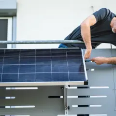 Mann montiert Solarmodul auf einem Balkongeländer.