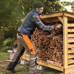 Mann stapelt Holz in einem Holzunterstand. Die Genehmigung für den Holzunterstand ist erteilt, und das Brennholz wird für den Winter vorbereitet.