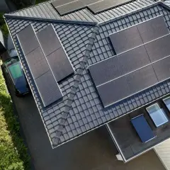 Dach mit Solarmodulen, ein schwarzes Auto und grüne Bäume. Die **agri pv voraussetzungen** sind erfüllt für dieses sonnenbeschienene Haus.