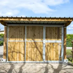 Ein mobiler Pferdestall ohne Baugenehmigung, aus Holz und Metall, mit Dach und Türen, ideal für flexible Pferdeunterbringung.