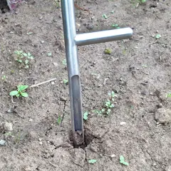 Ein Werkzeug zum Bodenproben ziehen steckt im trockenen Erdreich. Kleine grüne Pflänzchen sprießen zwischen den Rissen im Boden.