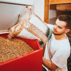 Mann füllt Holzpellets in einen Behälter. Die Pellets preisentwicklung ist ein wichtiges Thema für Heizungsbesitzer.