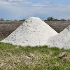 Zwei große Haufen weißes Material, vielleicht Kalkstickstoff, liegen auf einem Feld. Der **Kalkstickstoff Verbot** könnte die Ursache für diese Lagerung sein.