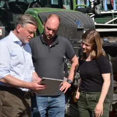 Drei Personen besprechen auf einem Tablet die **Pauschalierung in der Landwirtschaft** vor einem grünen Traktor.