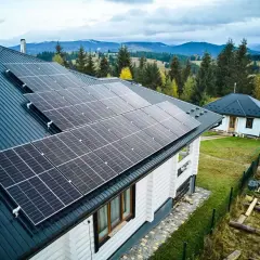 Häuser mit Solarmodulen auf dem Dach, bereit, Solarstrom zu verkaufen. Im Hintergrund bewaldete Hügel.