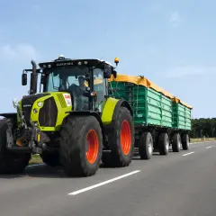 Ein Claas Arion Traktor mit Anhängern fährt auf der Straße. Der Fahrer hat die Fahrerlaubnis L und transportiert landwirtschaftliche Güter.
