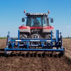 Traktor mit einem blauen Gerät für pfluglose Bodenbearbeitung auf einem Feld unter blauem Himmel.