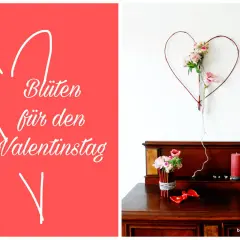 Blumen für den Valentinstag: Ein Herz aus Zweigen mit Blüten hängt über einem Holzmöbel mit Kerzen und Blumen.
