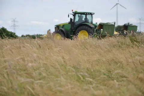 Grüner Traktor mit Anhängern im Feld, bereit für die Ernte. Die Kfz-Steuer für diesen Traktor ist ein wichtiger Faktor für Landwirte.