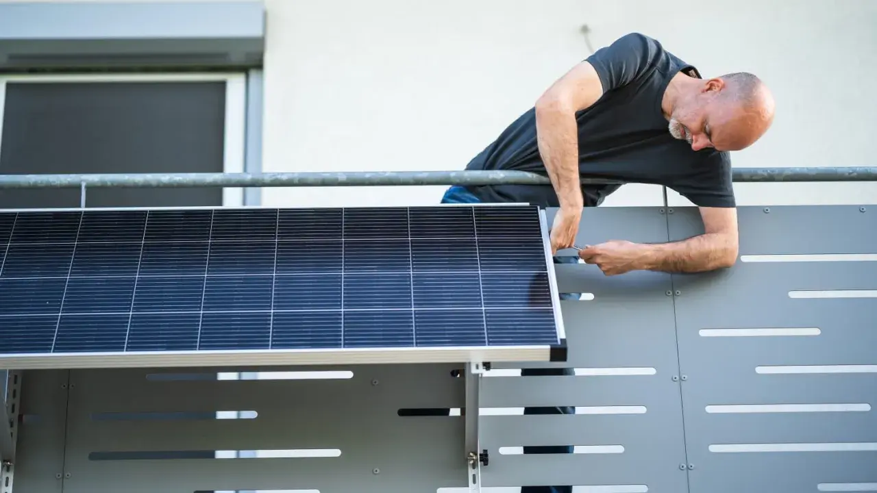 Mann montiert Solarmodul auf einem Balkongeländer.