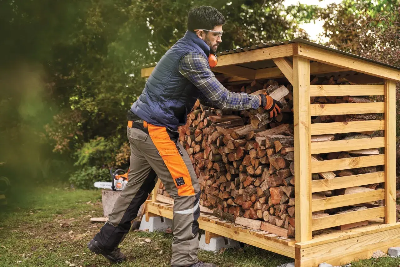 Mann stapelt Holz in einem Holzunterstand. Die Genehmigung für den Holzunterstand ist erteilt, und das Brennholz wird für den Winter vorbereitet.