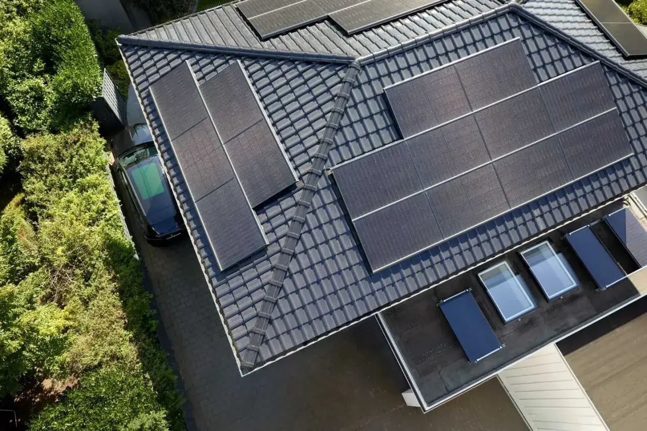 Dach mit Solarmodulen, ein schwarzes Auto und grüne Bäume. Die **agri pv voraussetzungen** sind erfüllt für dieses sonnenbeschienene Haus.