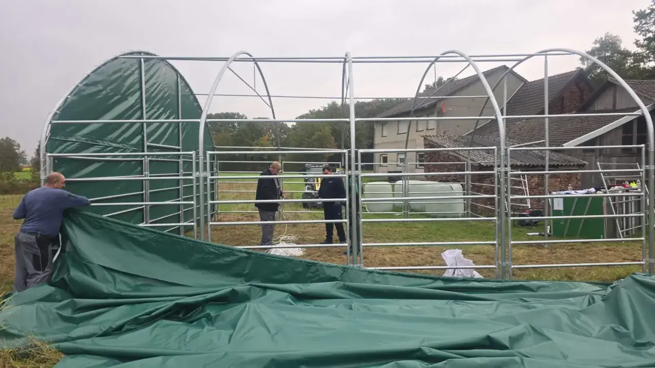 Aufbau einer 100 qm Halle genehmigungsfrei in Bayern. Männer montieren das grüne Dach einer Leichtbauhalle.