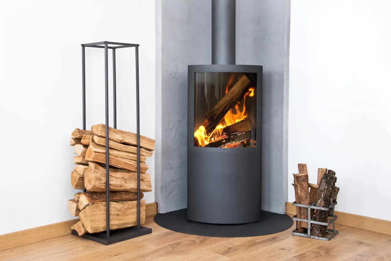 Moderner Kamin mit brennendem Holz. Ein Stapel Holz daneben. Diskussionen über ein holzheizung verbot sind angesichts dieser gemütlichen Szene unwahrscheinlich.