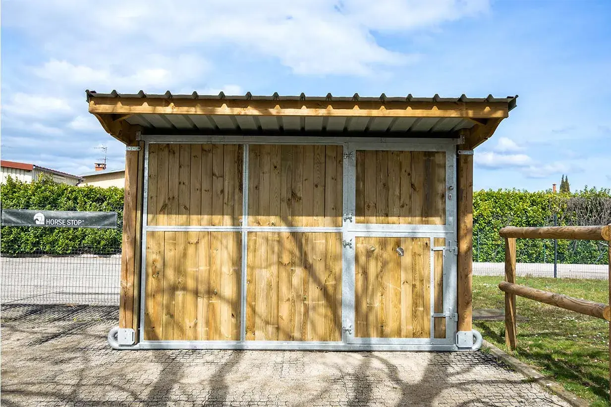 Ein mobiler Pferdestall ohne Baugenehmigung, aus Holz und Metall, mit Dach und Türen, ideal für flexible Pferdeunterbringung.