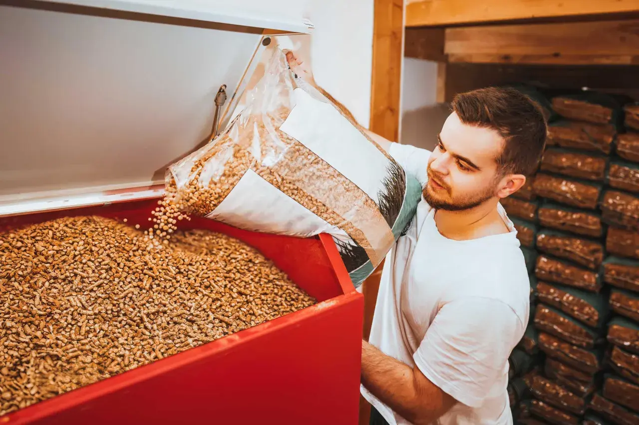 Mann füllt Holzpellets in einen Behälter. Die Pellets preisentwicklung ist ein wichtiges Thema für Heizungsbesitzer.