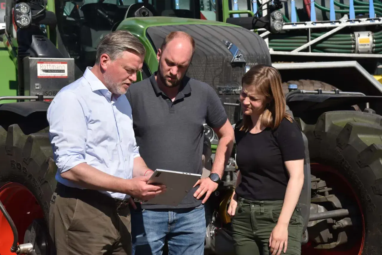 Drei Personen besprechen auf einem Tablet die **Pauschalierung in der Landwirtschaft** vor einem grünen Traktor.