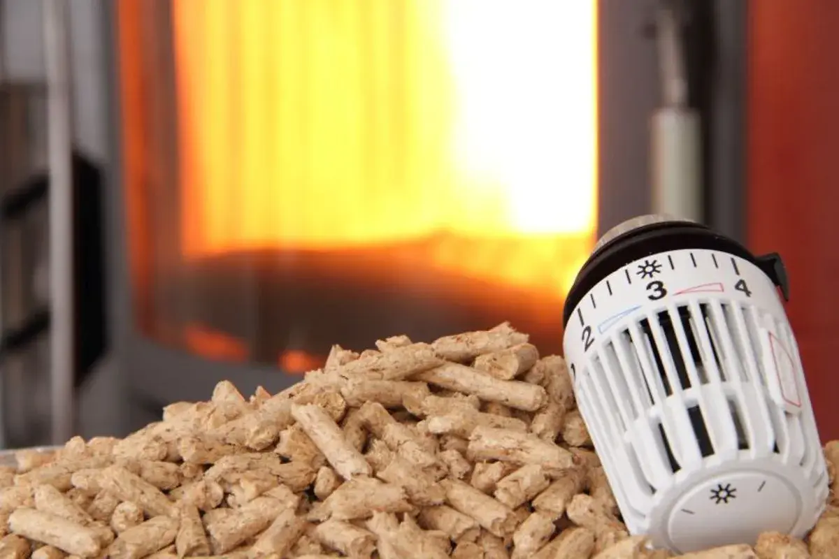 Holzpellets vor einem Kaminfeuer, daneben ein Thermostat zur CO2-Steuer.