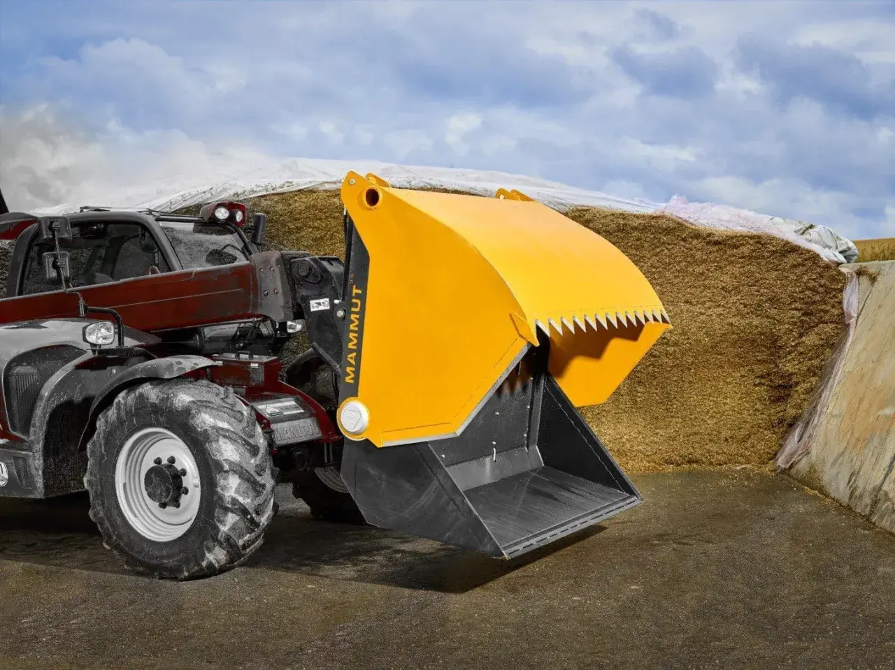 Ein Teleskoplader mit gelber Schaufel steht vor einem großen Silo in der Landwirtschaft.
