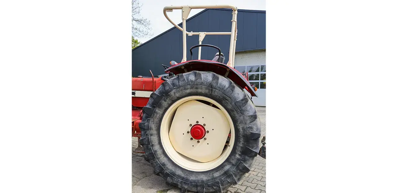 Roter Traktor mit großem Reifen und hellem Felgenhorn. Ein H-Kennzeichen ist am Traktor angebracht.