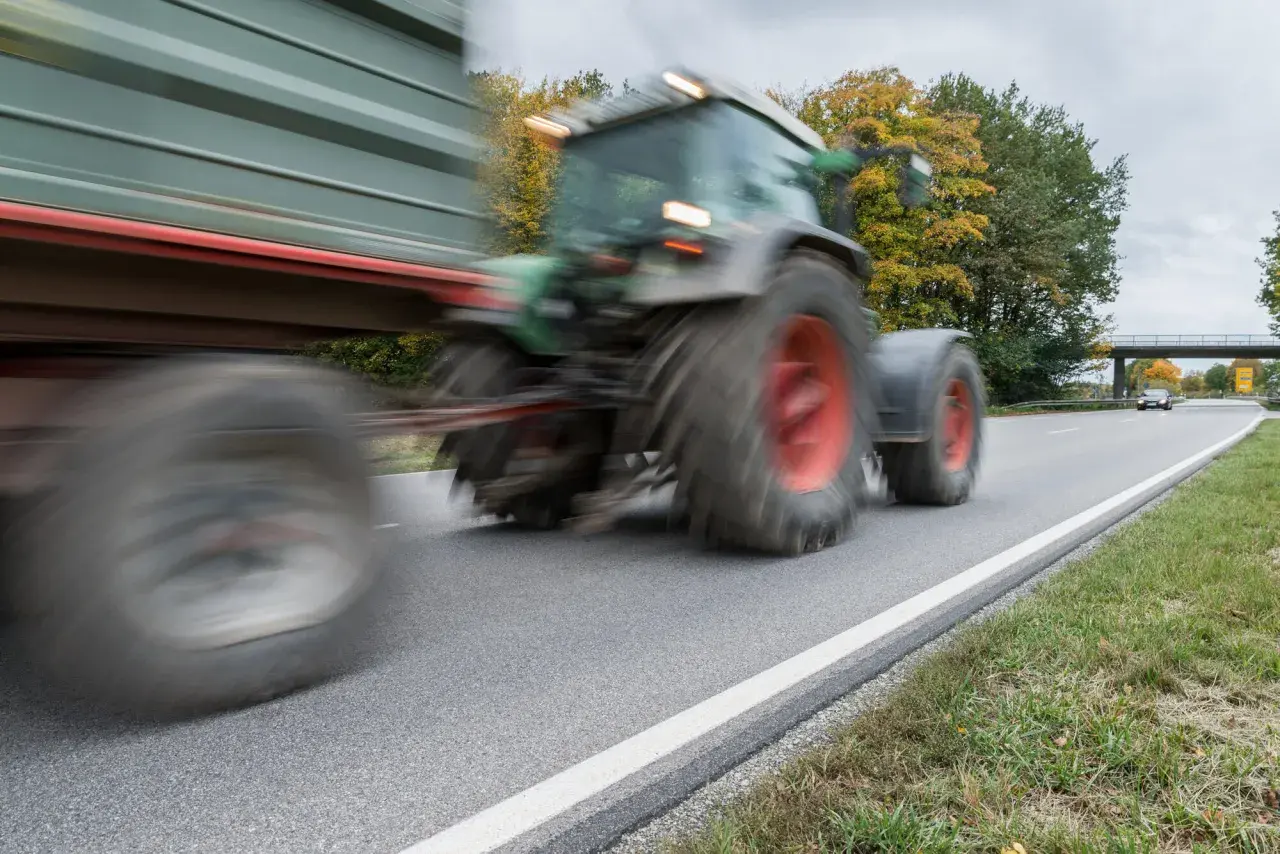 Ein Traktor mit Anhänger fährt auf einer Landstraße. Ab wann darf man Traktor fahren? Das ist eine wichtige Frage für junge Landwirte.