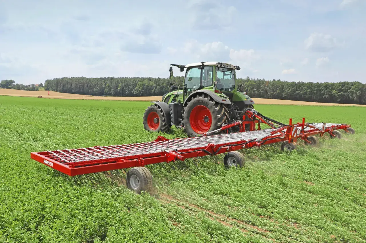 Grüner Traktor mit breiter Horsch-Maschine, die über ein Feld fährt, um das Getreide zu hacken.