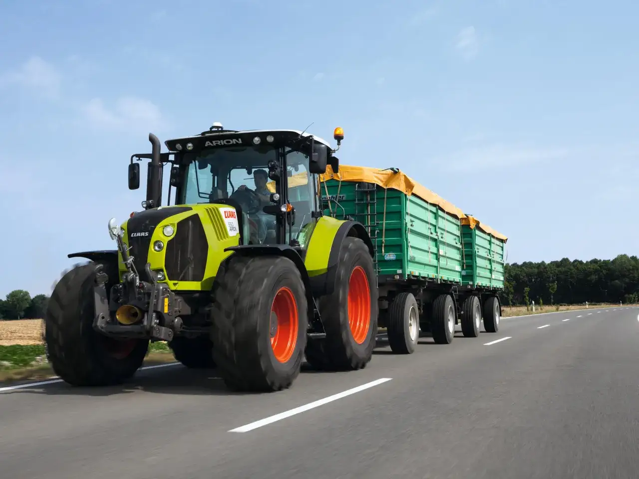 Ein Claas Arion Traktor mit Anh&auml;ngern f&auml;hrt auf der Stra&szlig;e. Ab wann darf man Traktor fahren? Mit 16 Jahren mit speziellem F&uuml;hrerschein.