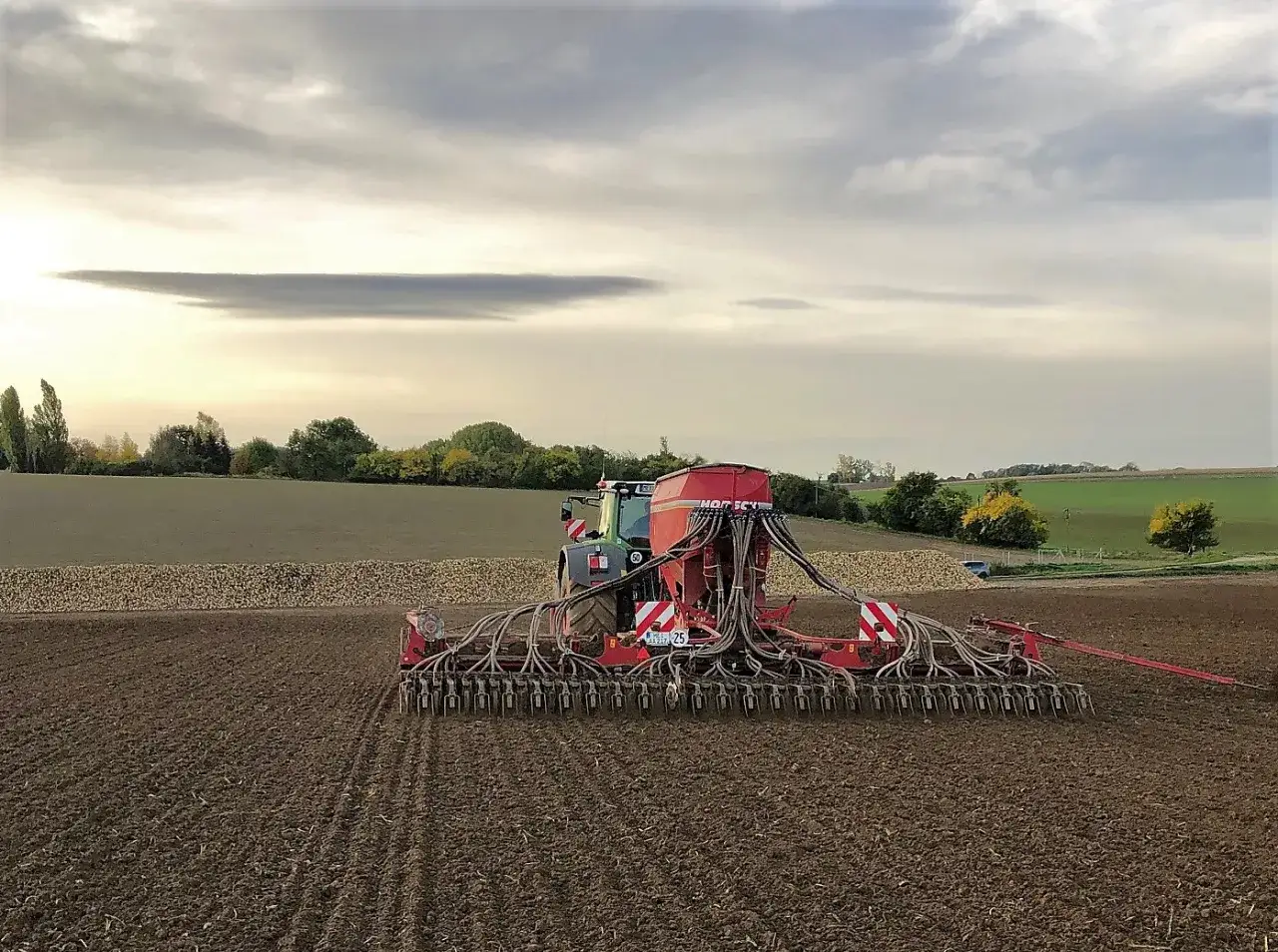 Traktor mit Sämaschine bei der Aussaat Winterweizen auf einem Feld. Der Himmel ist bewölkt.