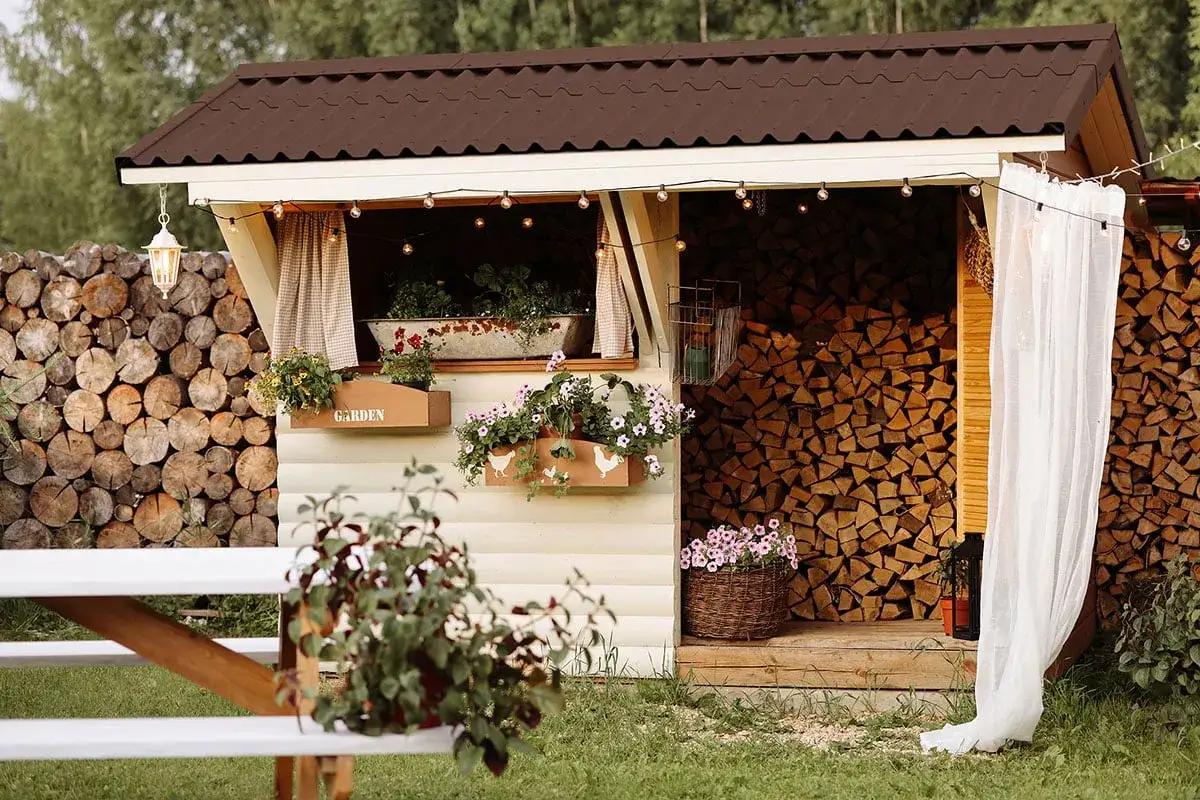 Gemütliche Hütte mit Blumenkästen und Lichterketten. Links und rechts ist Holz lagern, bereit für den Winter.