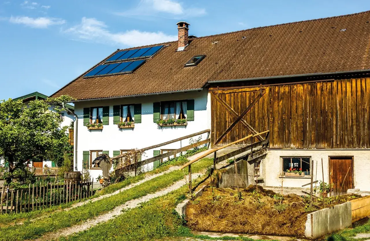 Ein Bauernhof mit Solaranlagen auf dem Dach und einem großen Holztor. Der Altenteiler Landwirtschaft genießt die Sonne.