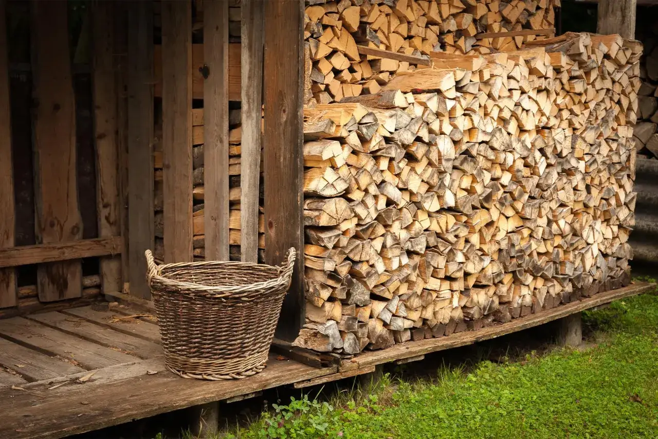 Ein Korb steht neben einem Holzstapel. Das Holz, vermutlich Esche, wartet auf seinen Einsatz als Brennmaterial mit hohem Brennwert.